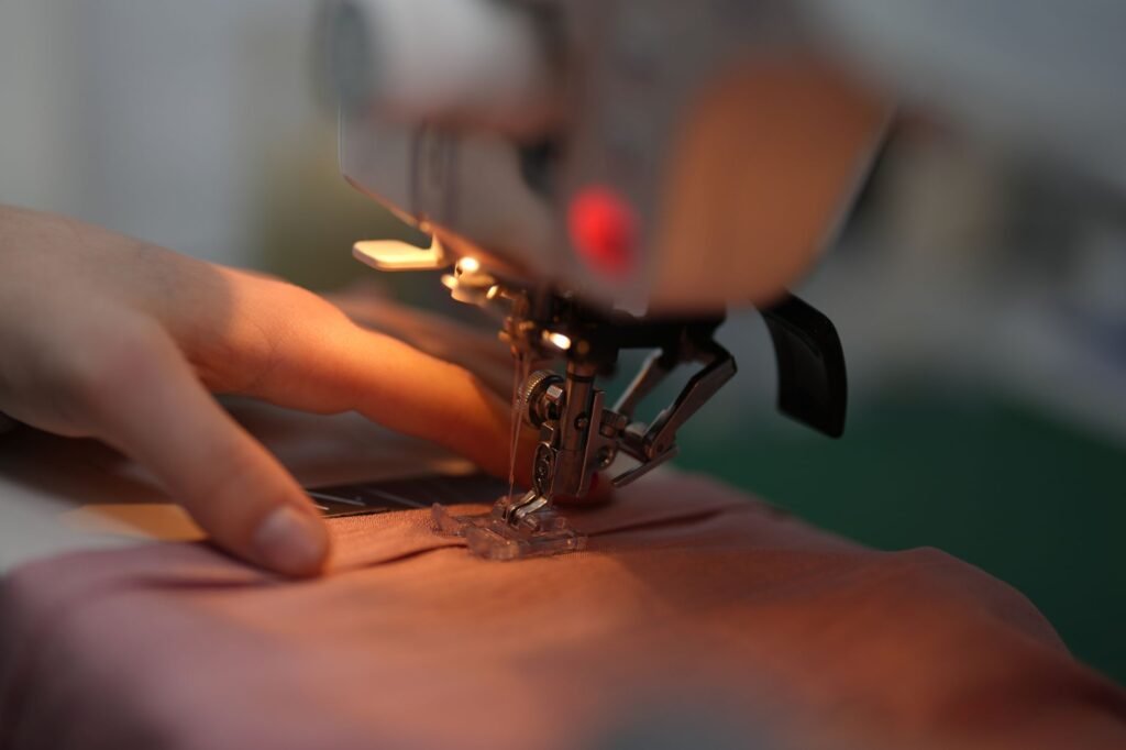 Una mano guía la tela bajo el prensatelas iluminado de una máquina de coser