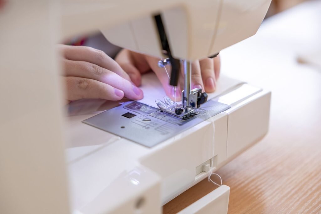 Manos guiando una tela bajo la aguja de una máquina de coser blanca